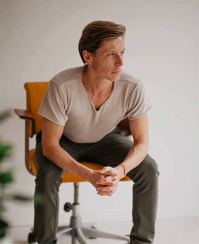 Seb Gamelkoorn of Primal Yoga sitting on a yellow office chair, leaning forward with hands clasped