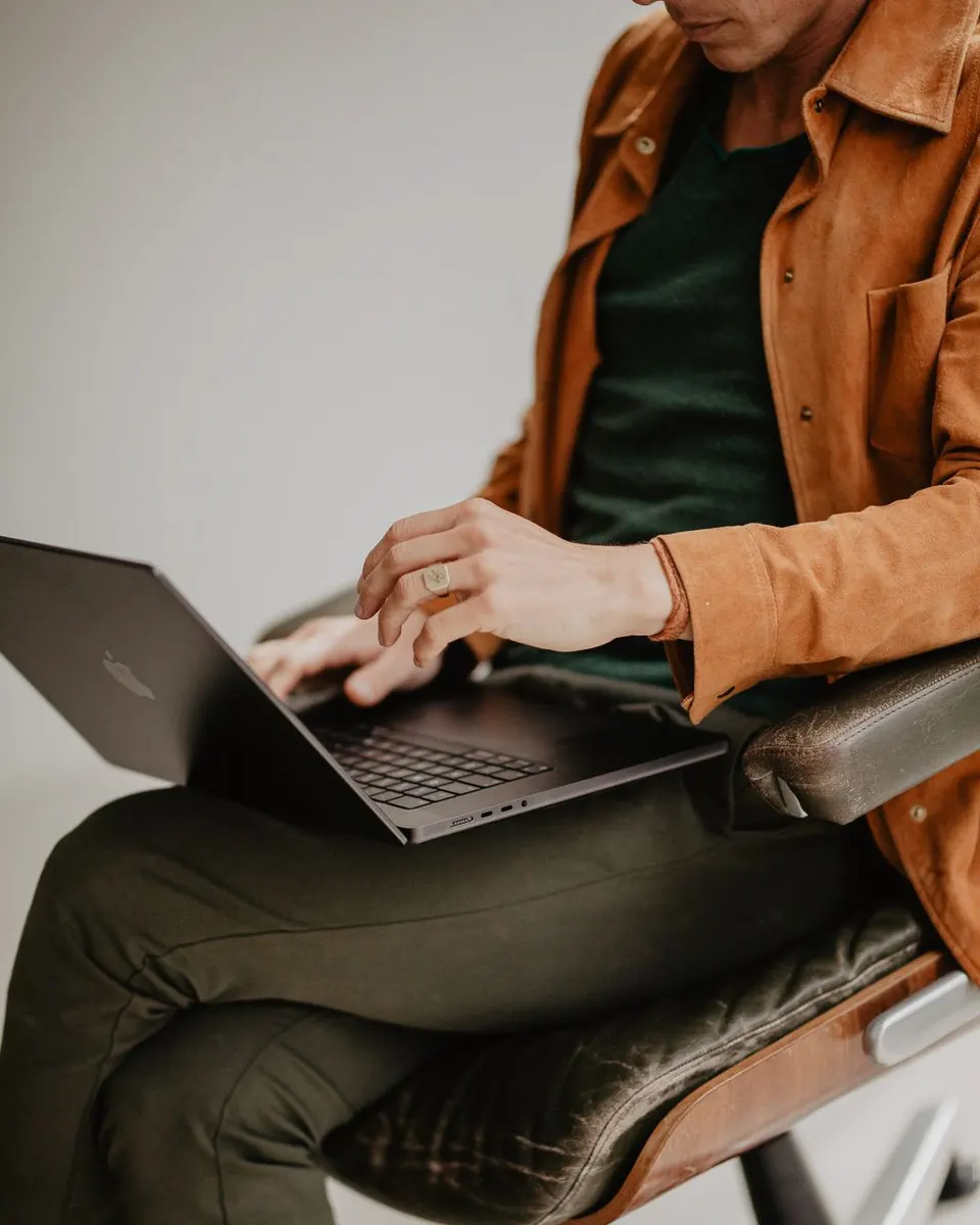 Seb of Primal Yoga sitting on an office chair with a laptop on crossed legs: the long hours of sitting the 10-minute desk reset helps undo